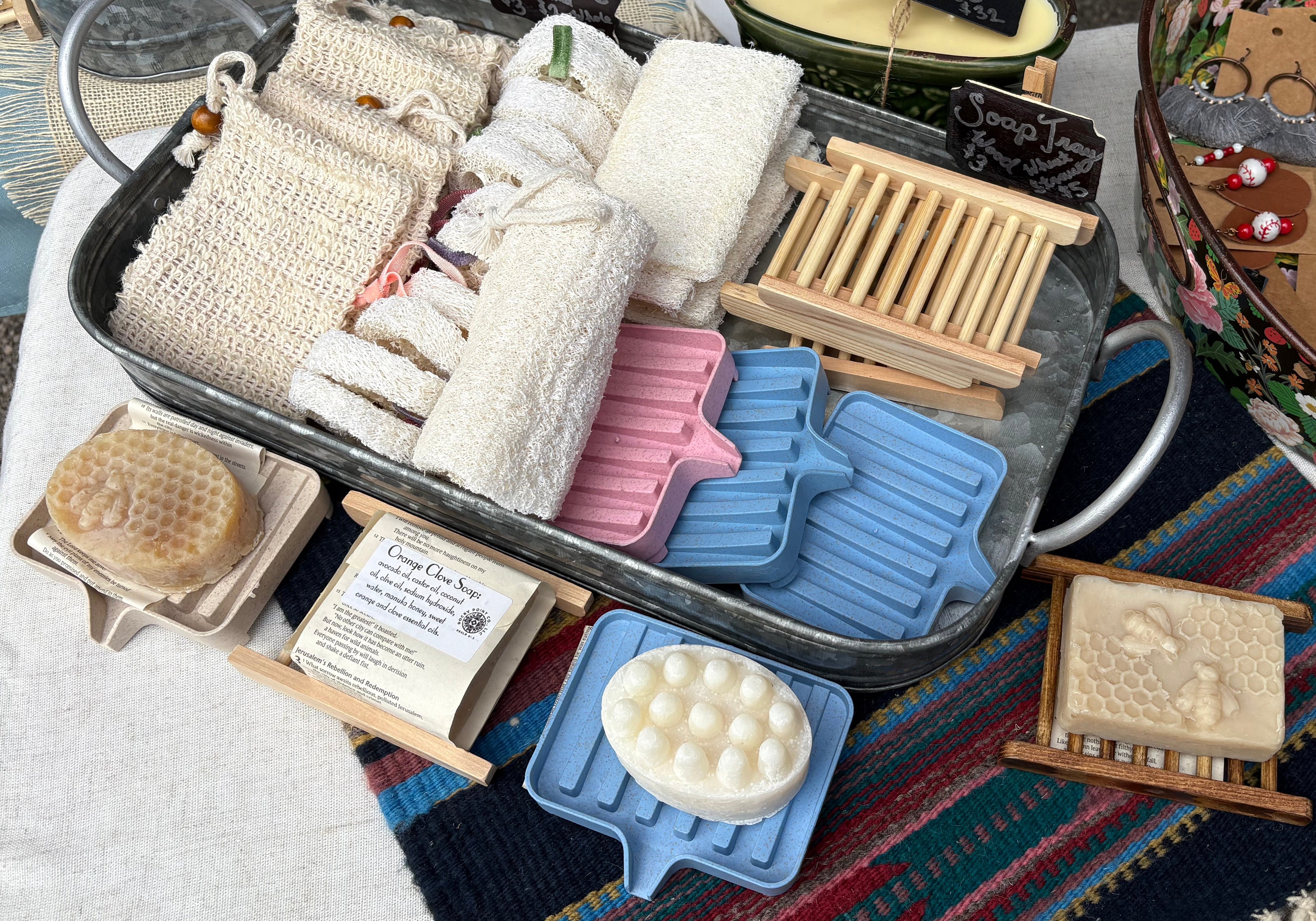 Collection of soaps, candles, and decorative items on a table with a colorful blanket underneath.