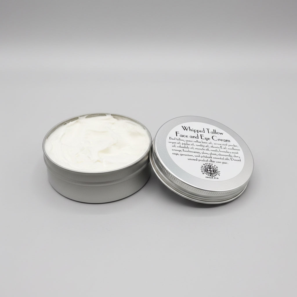 Whipped tallow face and eye cream in a metal tin on a patterned fabric background